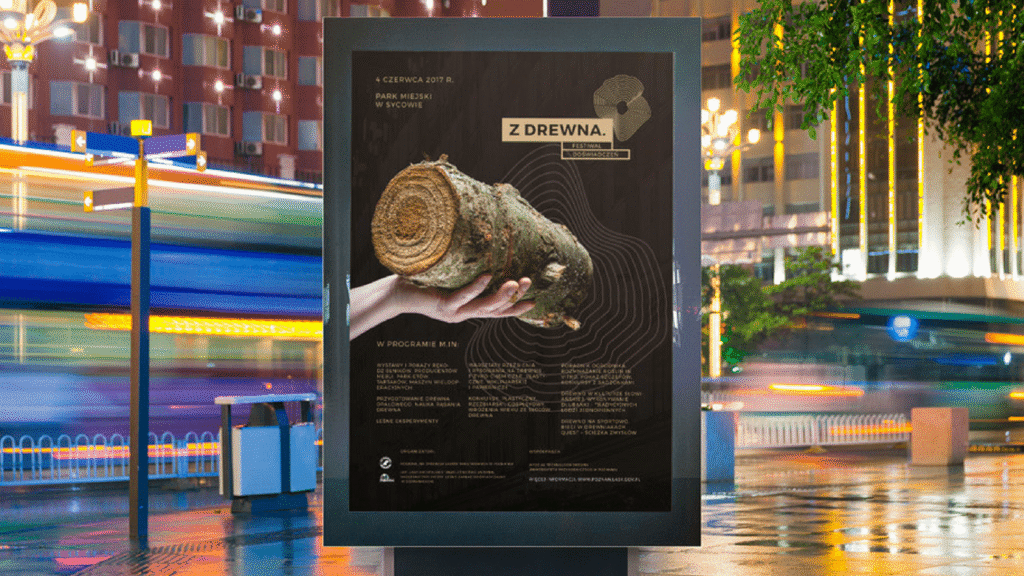 Plakat festiwalu na citylight w mieście nocą, przedstawiający drewno w dłoni człowieka.